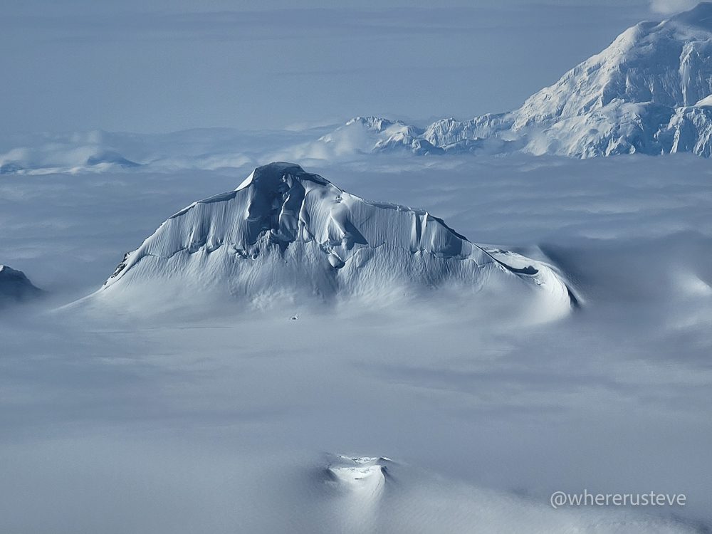 a mountain covered in snow and ice rises out of an icefield in Kluane national park, while flying toward Mount Logan