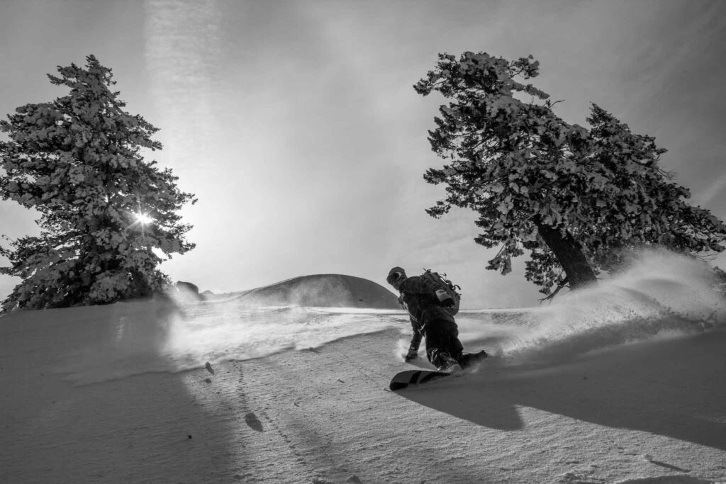 A snowboarder makes a big turn in powder, black and white image